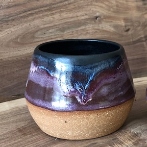 May include: A ceramic mug with a dark brown, purple, and blue glaze. The mug has a rounded shape and a wide base.