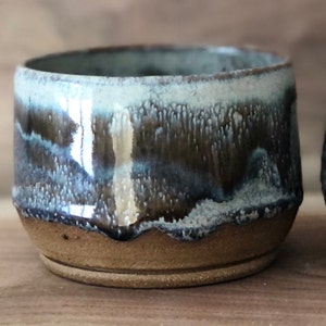 May include: A small, brown ceramic bowl with a blue and white glaze. The bowl has a slightly rounded bottom and a wide rim.
