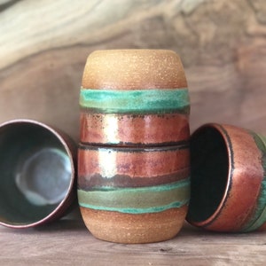 May include: Three ceramic mugs with a brown, copper, and green striped design. The mugs are stacked on top of each other.