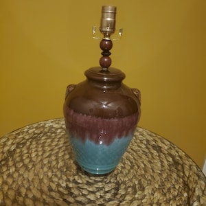 Puede incluir: Una lámpara de cerámica marrón y azul con una base de madera y una pantalla de metal dorado.