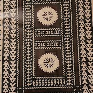 May include: A rectangular textile featuring a dark brown background with a repeating white pattern. The design includes borders of triangles, zig-zag lines, and two central circular floral motifs separated by a horizontal band of geometric shapes.