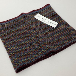 May include: A multi-colored cashmere neck warmer with a textured pattern. The neck warmer features a tag that reads "cashmere". The edges are a deep burgundy color, with a blue and green pattern throughout the fabric.