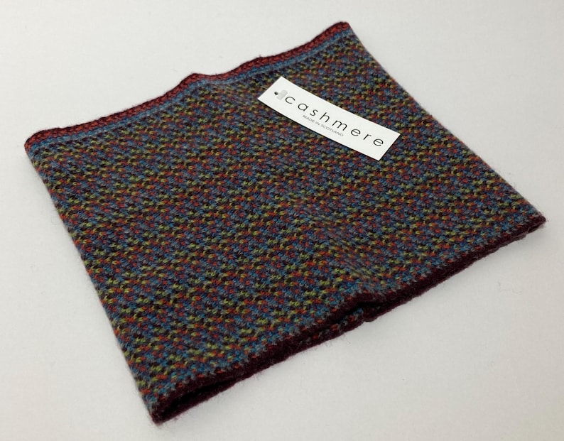 May include: A multi-colored cashmere neck warmer with a textured pattern. The neck warmer features a tag that reads "cashmere". The edges are a deep burgundy color, with a blue and green pattern throughout the fabric.