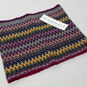 May include: A colorful cashmere neck warmer with a zig-zag pattern in shades of purple, blue, yellow, and green. The edge is a deep red. A tag with the word "cashmere" is attached.