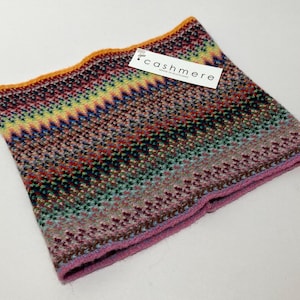 May include: A colorful cashmere neck warmer with a zig-zag pattern in shades of red, green, blue, and yellow. The edges are trimmed with orange and pink. A tag that says "cashmere" is attached.