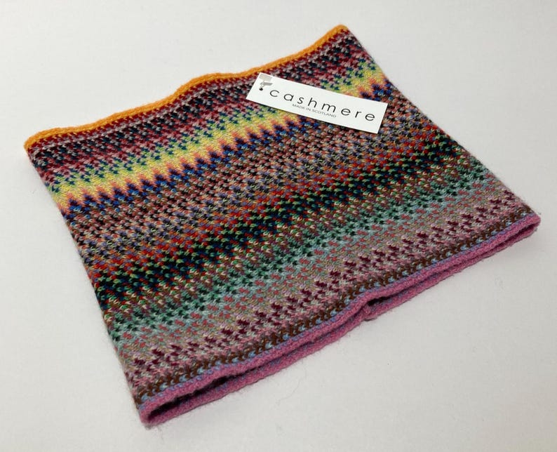 May include: A colorful cashmere neck warmer with a zig-zag pattern in shades of red, green, blue, and yellow. The edges are trimmed with orange and pink. A tag that says "cashmere" is attached.