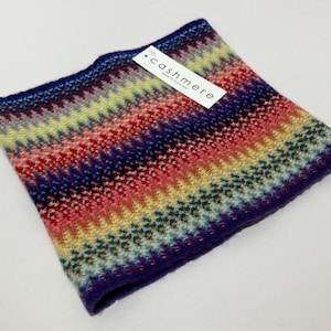 May include: A colorful cashmere neck warmer with a chevron pattern in shades of blue, red, yellow, and green. The label reads "cashmere". The neck warmer is a cozy accessory.