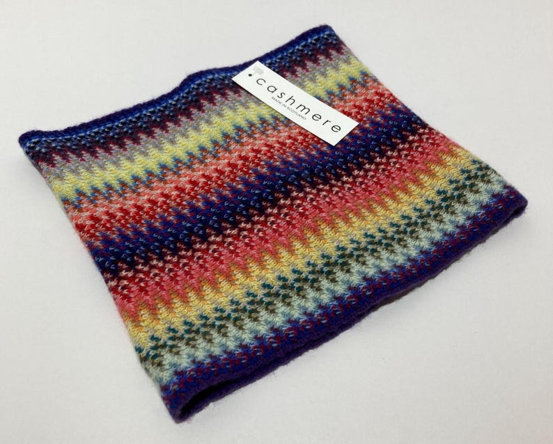 May include: A colorful cashmere neck warmer with a chevron pattern in shades of blue, red, yellow, and green. The label reads "cashmere". The neck warmer is a cozy accessory.