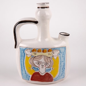 May include: White ceramic pitcher with a brown handle and a spout. The pitcher is decorated with a colorful illustration of a woman carrying a basket of fruit on her head.