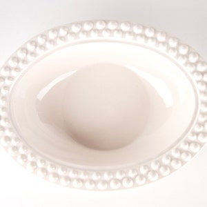 May include: A white oval ceramic bowl with a raised beaded rim.