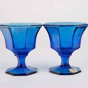 May include: Two cobalt blue glass pedestal bowls with a hexagonal base and a fluted design.