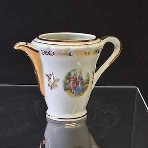 Peut inclure: Un pot à crème en porcelaine blanche avec un bord, une anse et un bec verseur dorés. Le corps est orné d'un médaillon circulaire représentant deux personnages en costumes d'époque, agrémenté de motifs floraux en feuille d'or.