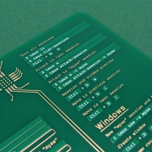 May include: A green printed cheat sheet with gold lettering showing commands for the tmux terminal multiplexer. The commands include "Show all sessions", "Attach to last session", "Attach to "myse" session", "Session and window preview", "Move to previous session", "Move to next session", and "Windows".