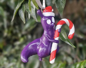 May include: Purple Christmas ornament shaped like a creature wearing a Santa hat and holding a candy cane.