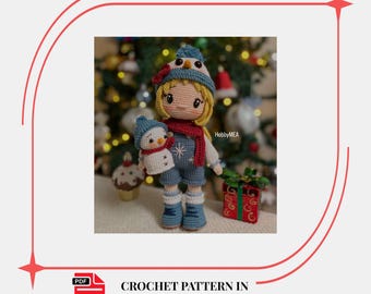 May include: A crocheted doll named Layla, wearing a blue hat, overalls, and boots, holding a snowman doll. The doll has blonde hair and a red scarf. A gift box and cupcake are in the background. The text "CROCHET PATTERN IN ENGLISH" is also visible.