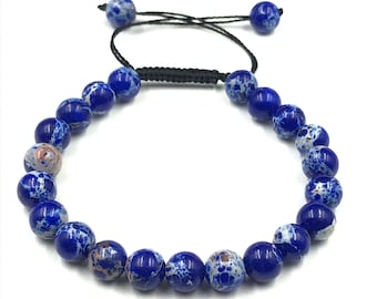 May include: A beaded bracelet featuring round, polished stones in shades of deep blue and white with occasional brown marbling. The beads are strung on a black cord with an adjustable sliding knot closure, finished with two smaller blue beads at the ends.