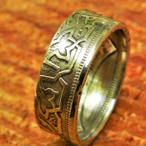 May include: A silver coin ring with an intricate design. The ring is made from a silver coin and has a smooth, polished finish.