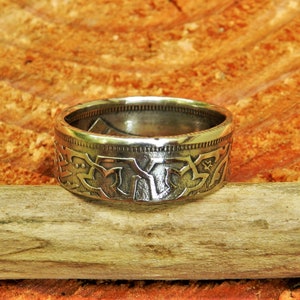 May include: A silver ring made from a repurposed coin. The ring features a detailed design of stylized leaves and flowers.