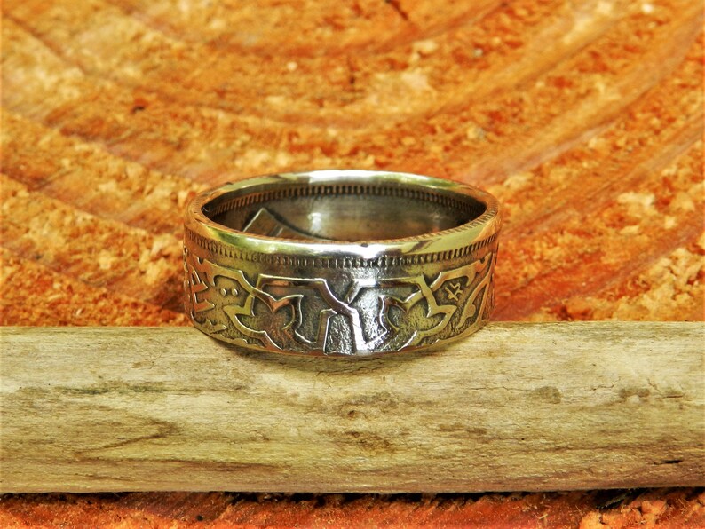 May include: A silver ring made from a repurposed coin. The ring features a detailed design of stylized leaves and flowers.
