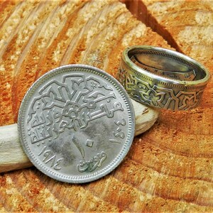 May include: A silver coin with Arabic script and the year 1942 on it. The coin is being used as a ring, with the edges bent to form a band.