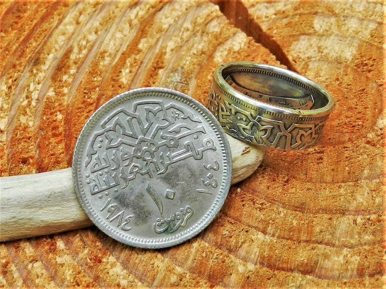 May include: A silver coin with Arabic script and the year 1942 on it. The coin is being used as a ring, with the edges bent to form a band.