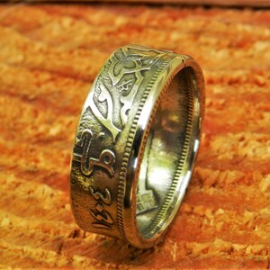 May include: A silver coin ring with intricate designs and Arabic script. The ring is made from a repurposed coin and has a smooth, polished finish.