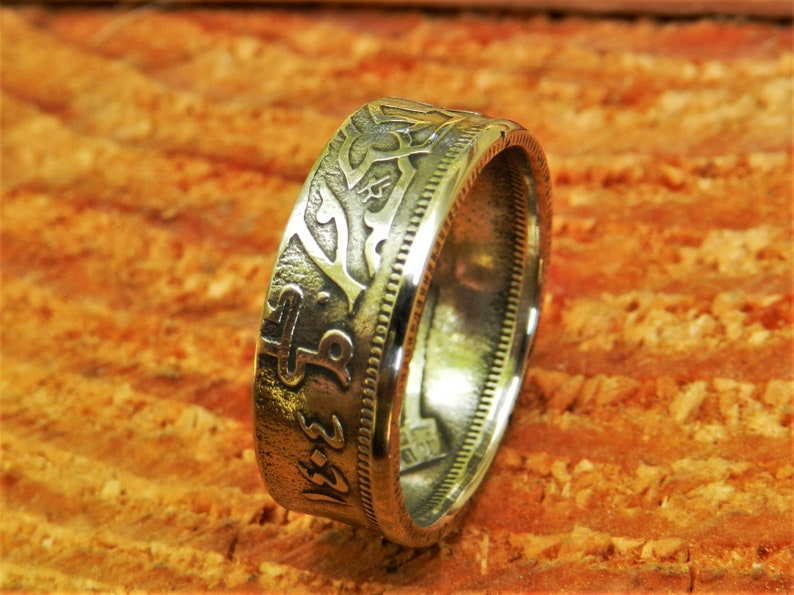 May include: A silver coin ring with intricate designs and Arabic script. The ring is made from a repurposed coin and has a smooth, polished finish.
