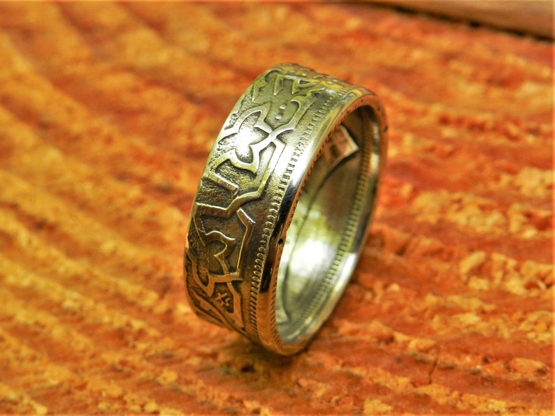 May include: A silver coin ring with an intricate design. The ring is made from a silver coin and has a smooth, polished finish.