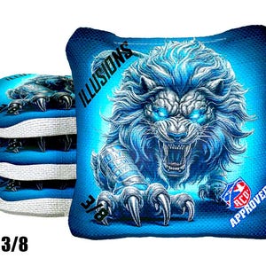 May include: Blue cornhole bag featuring a fierce lion illustration with glowing blue eyes and a detailed mane. The bag has the text "ILLUSIONS" and "3/8" printed on it, and is "ACO Approved". A stack of similar bags is visible.