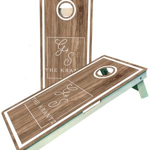 May include: Two wooden cornhole boards with a light brown wood grain design. Each board has a white border and a circular hole. The boards display the text "G+S THE KRANTZ" in a white, elegant font.