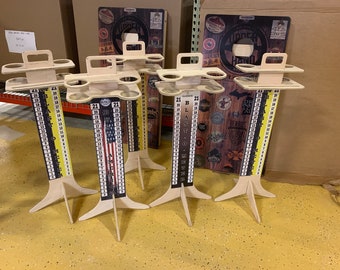 May include: Five wooden beer pong game sets with cup holders and scoreboards. The scoreboards feature different designs, including an American flag, a beer blast design, and a design with various beer logos. The sets are on a yellow floor.