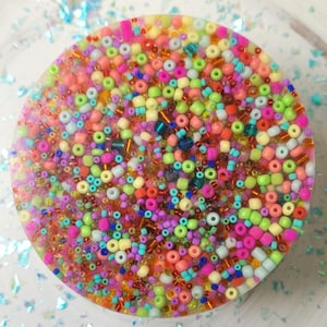 May include: A round, clear resin coaster with a colorful mix of small, multi-colored beads embedded inside. The beads are in shades of pink, orange, yellow, green, blue, and purple.