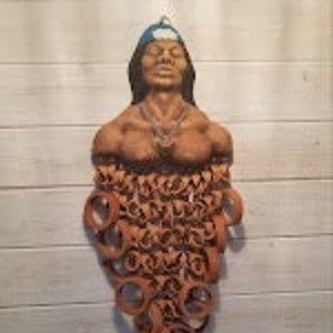 Peut inclure: Une sculpture en terre cuite d'un homme amérindien portant une coiffe bleue. La sculpture est en argile et a une surface texturée. L'homme porte un collier et a une expression paisible sur son visage.