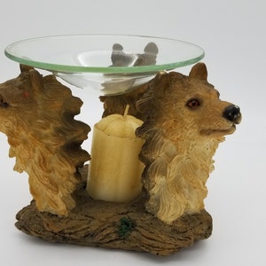 May include: A brown ceramic oil diffuser with two wolf heads on the sides. The diffuser has a glass dish on top and a candle holder in the centre.