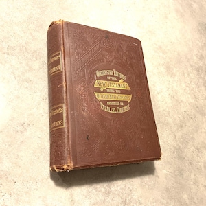 Puede incluir: Un libro encuadernado en cuero marrón con letras doradas en la portada. El título es "Contrasted Editions of the New Testament, Being the Old and New Versions Arranged in Parallel Columns".