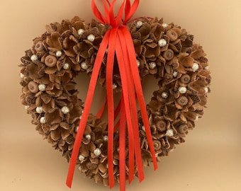 May include: A heart-shaped wreath made of pine cones and accented with silver beads. A red ribbon is tied at the top.