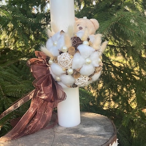 May include: A white candle with a brown ribbon and a decorative arrangement of white cotton balls, brown twigs, and a small brown teddy bear.