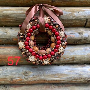 May include: A festive wreath with a brown ribbon, red ornaments, walnuts, and pinecones. The wreath is displayed against a rustic wooden background. The number "57" is visible in the lower left corner.
