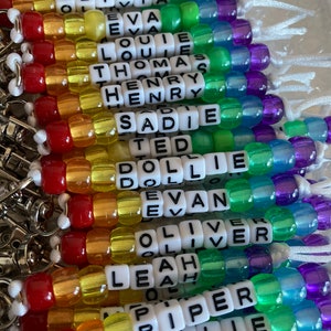May include: A rainbow of beaded keychains with different names spelled out on each one. The names include Alice, Holly, Olivia, Eva, Louie, Thomas, Henry, Sadie, Ted, Dollie, Evan, Oliver, Leah, Piper, Millie, and Sophie.
