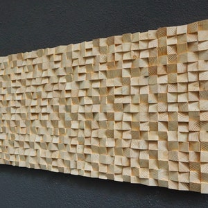 May include: A rectangular wooden wall art piece composed of numerous small, unevenly cut blocks. The blocks are arranged to create a textured, three-dimensional surface. The wood has a natural, light-brown color.