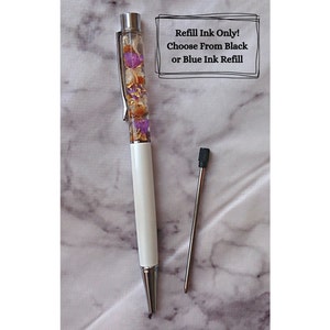 Peut inclure: Stylo blanc avec un corps transparent rempli de fleurs s&eacute;ch&eacute;es et de paillettes dor&eacute;es. Le stylo a un clip argent&eacute; et une recharge d'encre noire. Le texte "Refill Ink Only! Choose From Black or Blue Ink Refill" est &eacute;crit sur un rectangle blanc.