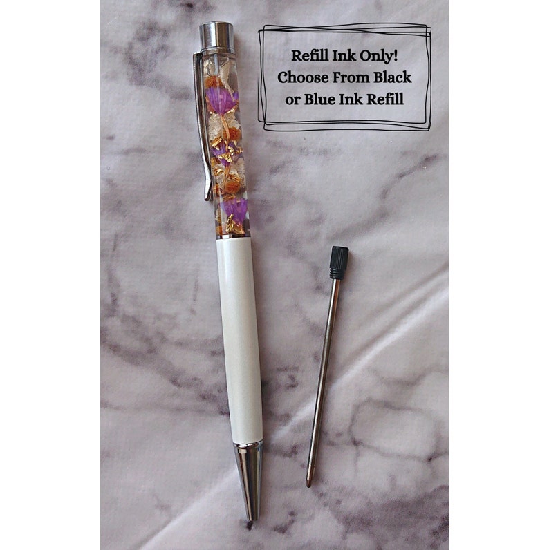 Peut inclure: Stylo blanc avec un corps transparent rempli de fleurs s&eacute;ch&eacute;es et de paillettes dor&eacute;es. Le stylo a un clip argent&eacute; et une recharge d'encre noire. Le texte "Refill Ink Only! Choose From Black or Blue Ink Refill" est &eacute;crit sur un rectangle blanc.