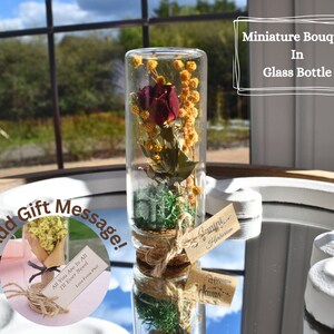 A bouquet of red rose, complemented with yellow mimosa and green moss, all placed beautifully in a glass cork bottle.