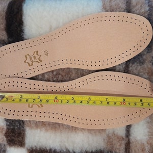 May include: A pair of beige leather insoles with a perforated pattern. The insoles are measured with a tape measure, showing a length of 10 inches. The insoles have the text "LEATHER" and "40" printed on them.
