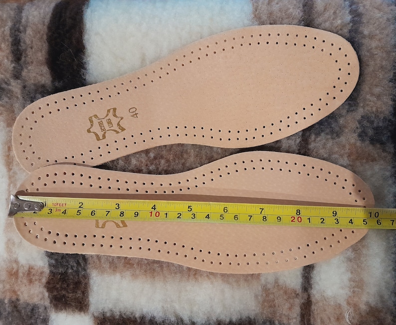 May include: A pair of beige leather insoles with a perforated pattern. The insoles are measured with a tape measure, showing a length of 10 inches. The insoles have the text "LEATHER" and "40" printed on them.