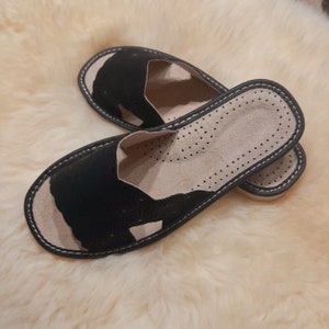 May include: A pair of black leather slippers with a perforated design and a white stitching detail. The slippers have a comfortable, cushioned insole.