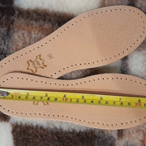 May include: A pair of brown leather insoles with a size 36 label. The insoles have a pattern of small holes and are measured with a tape measure, showing a length of 10 inches.