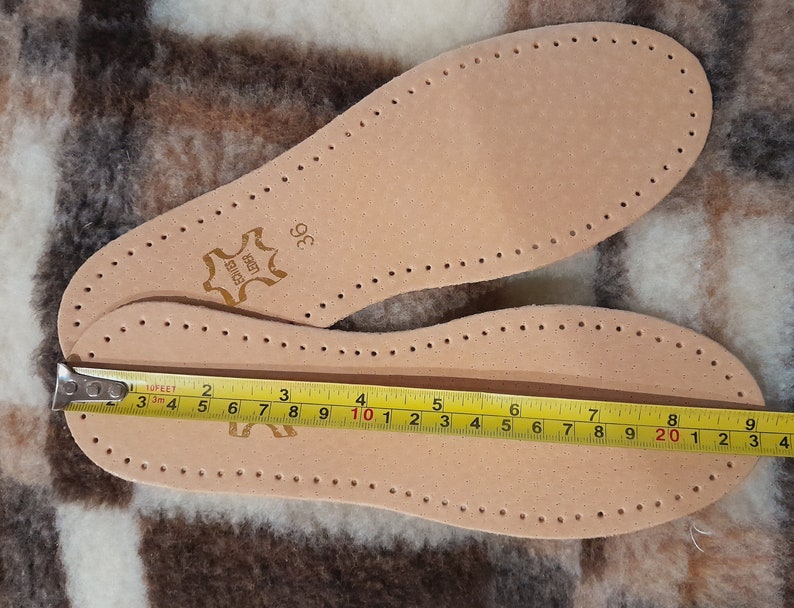 May include: A pair of brown leather insoles with a size 36 label. The insoles have a pattern of small holes and are measured with a tape measure, showing a length of 10 inches.
