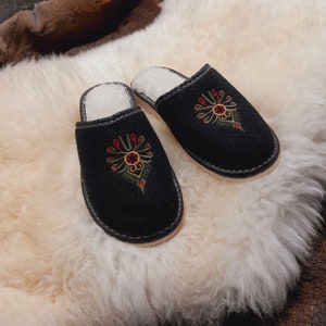 Könnte beinhalten: Ein Paar schwarze Hausschuhe mit gestickten Blumenmustern in Rot, Grün und Gelb. Die Hausschuhe haben ein weiches, flauschiges Futter und sind perfekt, um Ihre Füße warm und gemütlich zu halten.