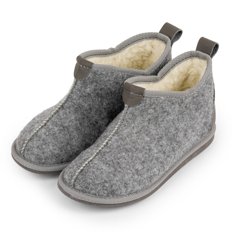May include: A pair of gray wool slippers with a brown leather trim. The slippers have a soft, fuzzy lining.